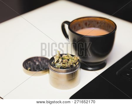 Cannabis Or Marijuana Flower In A Steel Grinder On A Desk, Next To A Cup Of Coffee And A Laptop.