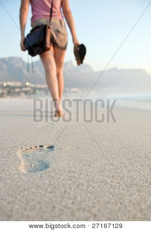 Ragazza cammina con le scarpe in mano lungo l'arenile.
