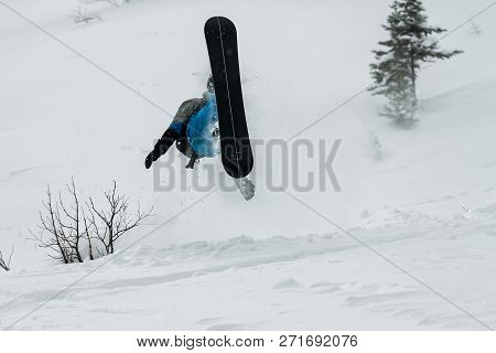 Snowboarder Freerider Jumping From A Snow Ramp On A Background Of Forest And Mountains