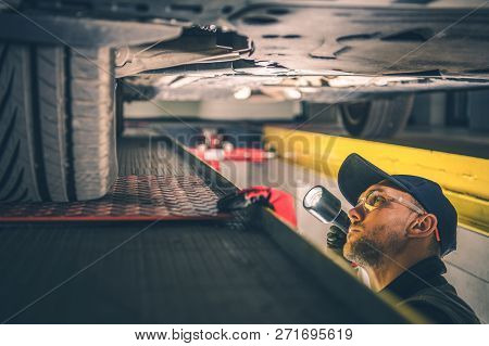 Car Suspension Issue. Caucasian Vehicle Mechanic With Flashlight Inspecting Car Undercarriage.
