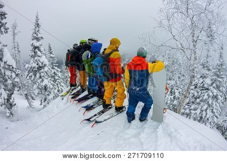 Group Team Of Free-riders Skiers, Snowboarders Stand On The Mountainside And Look Down