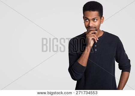 Contemplative Man With Beard And Dark Skin, Holds Chin, Looks Thoughtfully Somewhere, Dressed Casual