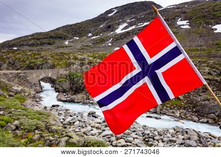 Norwegian Flag Waving Against Mountains Landscape. Travel, Holidays And Adventure Concept.