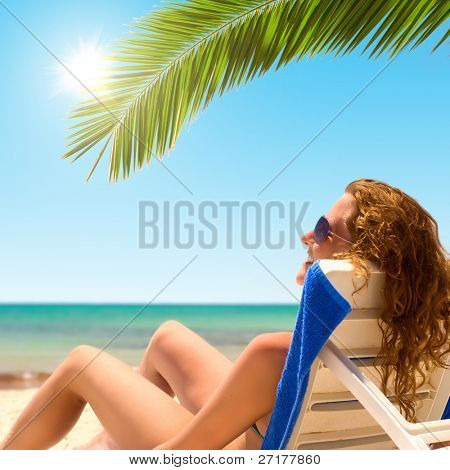 sexy žena sedí na chaise longue pod palmou
