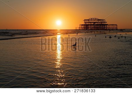 The Old Remains Of Brighton Pier Left Standing In Sea With Beautiful Waves, Seagulls And Local Peopl