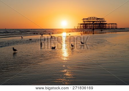The Old Remains Of Brighton Pier Left Standing In Sea With Beautiful Waves, Seagulls And Local Peopl