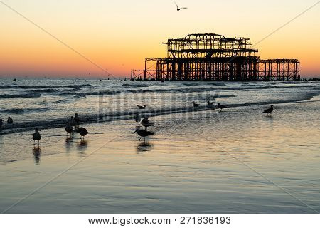 The Old Remains Of Brighton Pier Left Standing In Sea With Beautiful Waves, Seagulls And Local Peopl