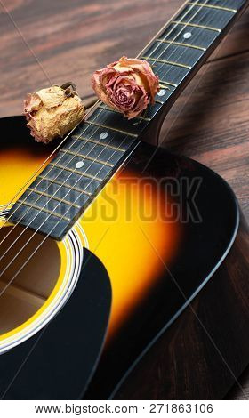 Acoustic Guitar With Dried Roses On The Wooden Table. Template For Advertising A Concert Of Memory O