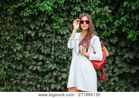 Close Up Image Of Happy Brunette Woman In Sunglasses And Red Bag Posing Sideways Outdoors