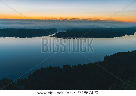 View From High Shore On Broad River. Riverbank With Forest Under Thick Fog. Dawn Reflected In Water.
