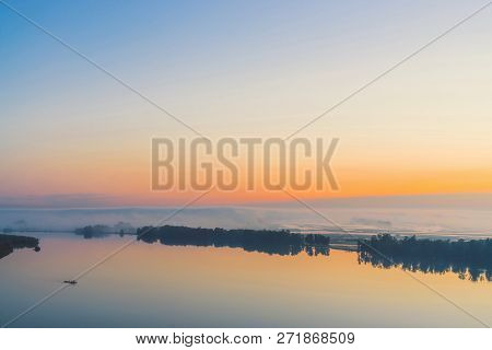 Broad Mystical River Flows Along Diagonal Shore With Silhouette Of Trees And Thick Fog. Gold Glow In