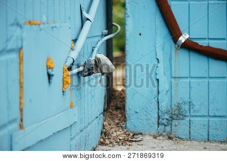 Blue Wall From Tiles With Cyan Closed Hatchway And Pipes Close Up. Background Of Wall Of Building Wi