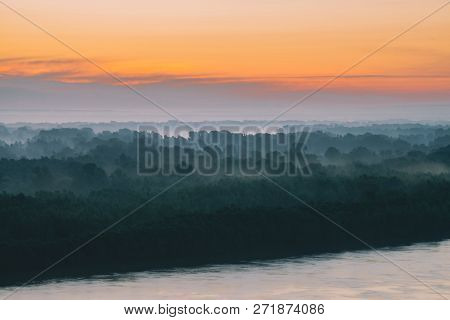 Mystical View On Riverbank Of Large Island With Forest Under Haze At Early Morning. Mist Among Layer