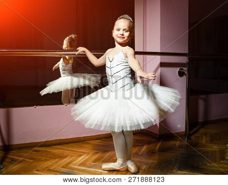 Portrait Of Smiling Young Ballerina In White Tutu And Pointes Posing Isolated In Dance Studio. Small