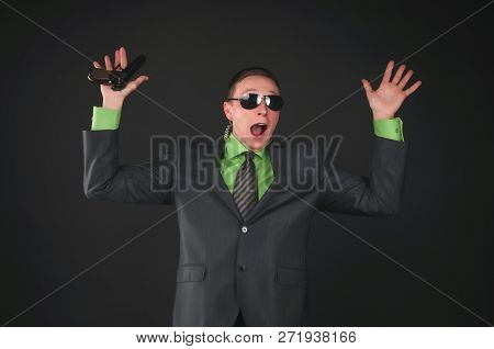 Scared Security Agent Is Surrender And Holding His Hand With A Gun Raised Up Isolated On Black Backg