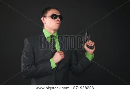 Arrogant Security Agent Is Posing With A Gun In Hand Like A Super Spy Isolated On Black Background.