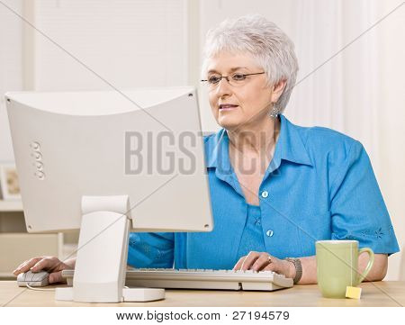Senior donna guardando il monitor del computer e digitando sulla tastiera