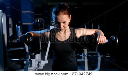 The Girl Is Engaged In The Gym. Exercise On The Deltoid Muscles With A Dumbbell.