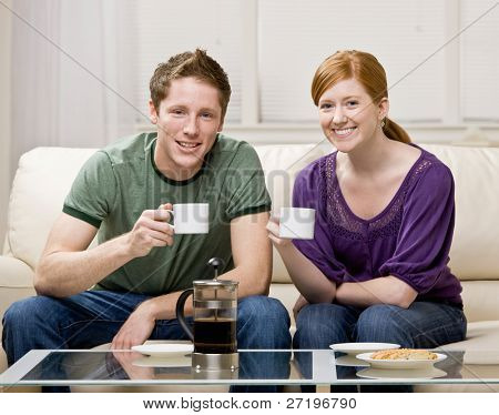 Счастливая пара, сидя на диване в гостиной, свежий кофе пить