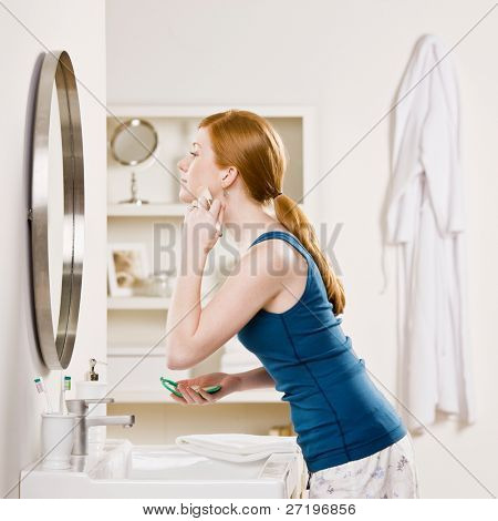 Woman in pajamas in bathroom applying blush with makeup brush