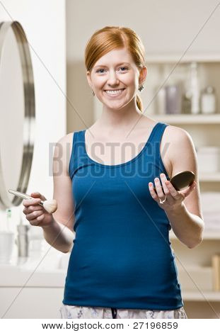 Woman in pajamas in bathroom applying blush with makeup brush