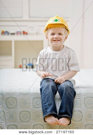 Unge barfodet dreng siddende på sengen i soveværelset iført hard-hat