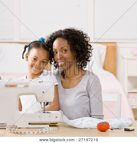 Donna creativa utilizzando la macchina da cucire per cucire vestiti per la figlia