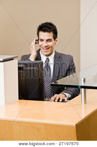 Male receptionist talking on telephone earpiece working at front desk
