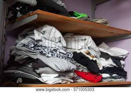 Piles Of Not Neatly Folded Clothes Of Different Colors On A Wooden Shelf