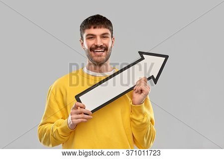 direction and people concept - happy smiling young man holding big white thick upwards arrow pointing to right over grey background
