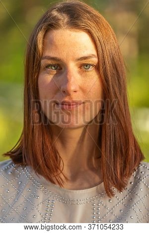 Portrait Of A Young Red-haired Girl, Girl Looking At The Camera And Smiling Shyly. Freckles On The F