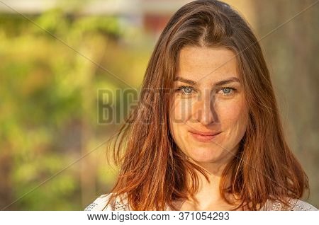 Portrait Of A Young Red-haired Girl, Girl Looking At The Camera And Smiling Shyly. Freckles On The F