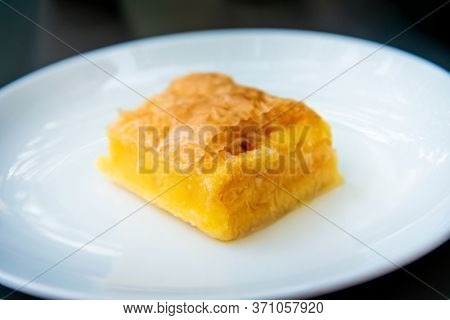 Delicious Greek sweet pastry named Galaktoboureko, made of semolina custard in filo, served with honey in white plate.