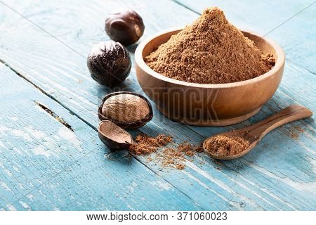 Whole Inshell Nut, Cracked And Nutmeg Powder In A Wooden Bowl And Spoon On Old Blue Rustic Backgroun
