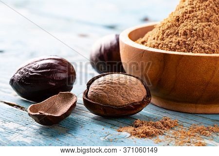 Whole Inshell Nut, Cracked And Nutmeg Powder In A Wooden Bowl And Spoon On Old Blue Rustic Backgroun