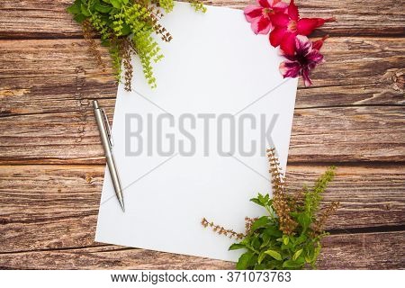 Conceptual Space For Text, Which Consists Of Blank Paper, Azalea, Basil Flowers,and Pens On A Wooden