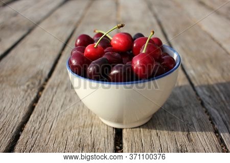 Ripe Black Cherries With Water Drops In A White Ceramic Bowl With A Blue Border On A Wooden Table Ba