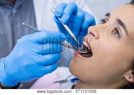 High angle view of dentist holding tools while examining woman at medical clinic