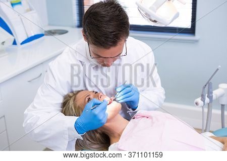 High angle view of dentist examining woman with dental equipments at medical clinic