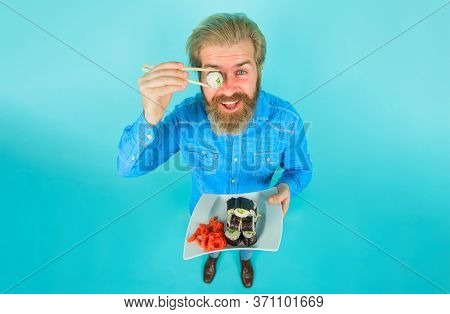 Seafood. Man Eating Sushi. Man Hold Piece Sushiroll In Front Of Eye. Man With Sushi On Chopstick. Su