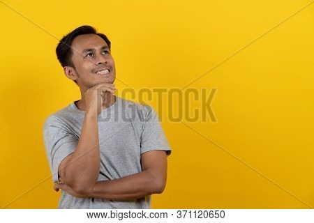 Cute Asian Man In Casual Thinking And Imagination Isolated On Yellow Background