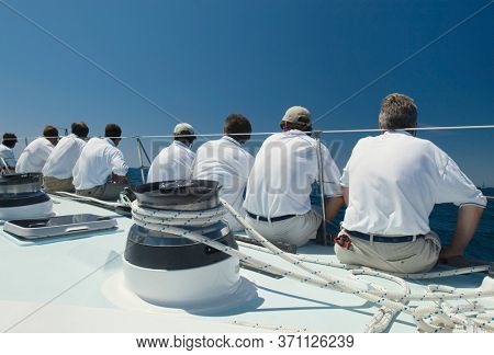 Sailing crew sitting on side of yacht on ocean back view