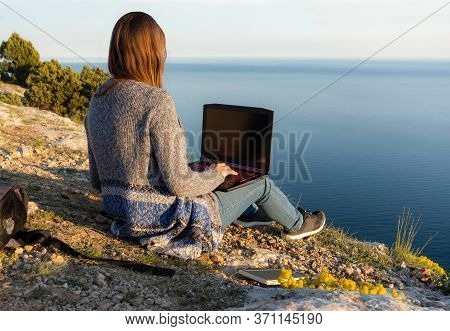 A Girl Is Working On A Laptop At The Top Of A Mountain. Remote Work And Training In Nature. Sea View