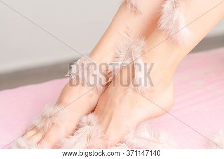 Close Up Of White Feathers Covers Smooth Legs Of Woman. Hair Removal And Body Care Concept.