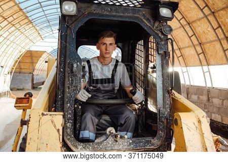A Man In Overalls Driving A Tractor. Worker Sitting On His Tractor
