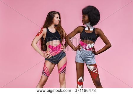 Kinesiology Taping. Two Young Female Athletes On Pink Background With Kinesiology Tape On Neck, Shou