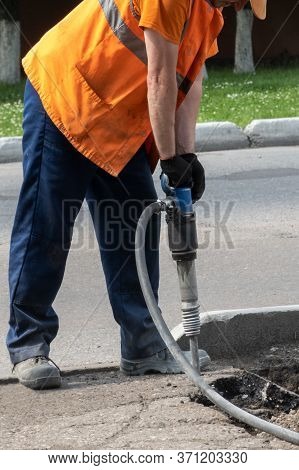 Dismantling Of The Road Surface. A Road Worker With Tension Is Hammering The Asphalt With A Jackhamm