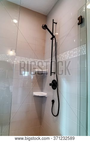 Black Round Shower Head On Tile Wall Of Shower Stall With Hinged Glass Door
