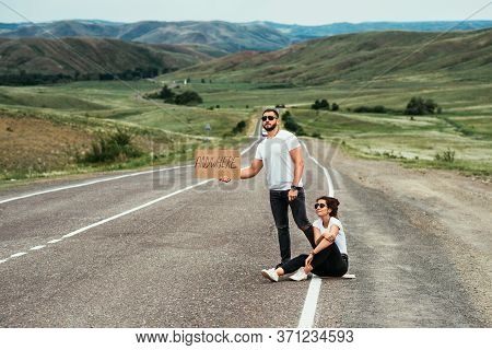 A Couple Hitchhiking. A Man And A Woman Catch A Car By The Road. A Young Couple Votes On The Road. A