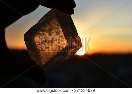 A Close Up Image Of Transparent Champagne Calcite Held Against A Glowing Orange Sunset.